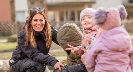 En pedagog och två barn sitter utomhus och skrattar