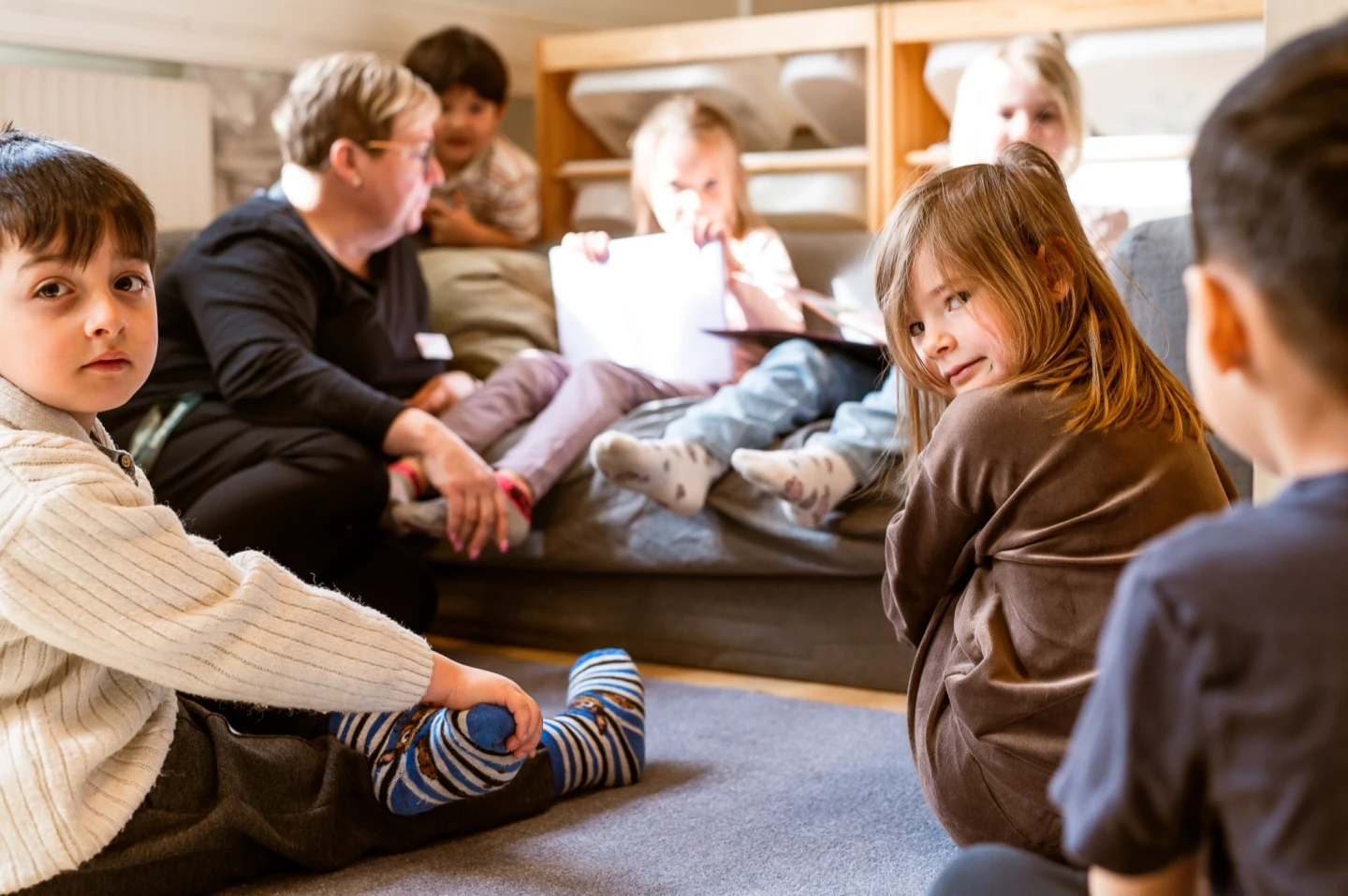 En grupp med barn sitter tillsammans med en vuxen på golvet i ett rum