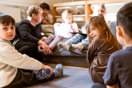 En grupp med barn sitter tillsammans med en vuxen på golvet i ett rum