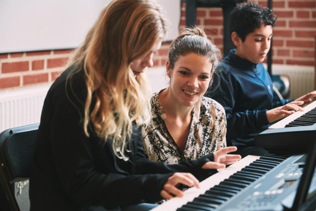 Två elever och en lärare vid ett piano.