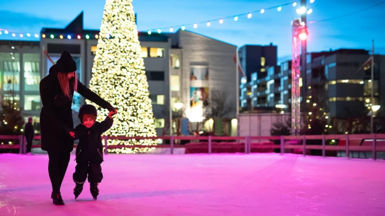 Kvinna och barn på isbanan på Sundstorget med den glimrande granen i bakgrunden