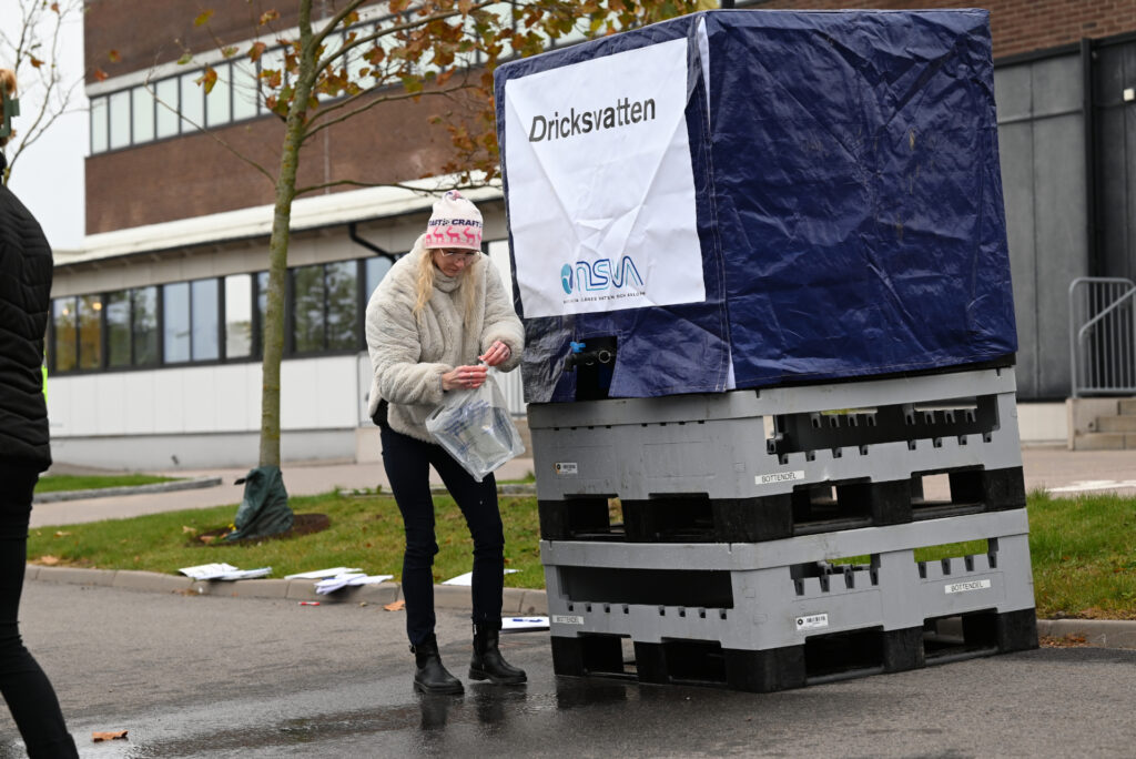 En person fyller på en enkel plastdunk vid en stor vattentank märkt med texten "Dricksvatten"