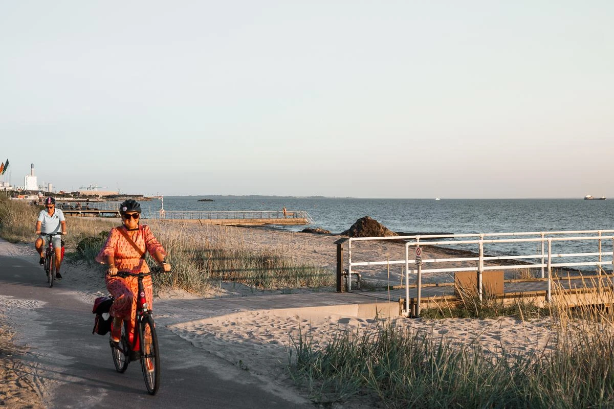 En kvinna och en man cyklar längs stranden i solnedgången.