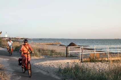En kvinna och en man cyklar längs stranden i solnedgången.