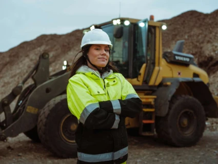 kvinna i hjäl som arbetar som anlägningsförare framför en traktor.