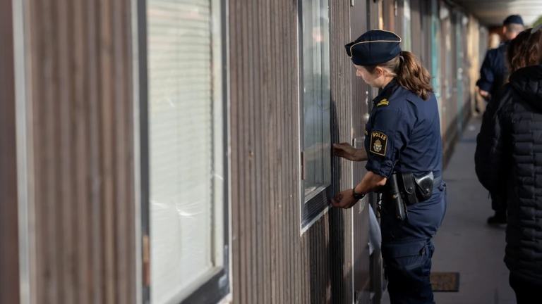 En polis står på en loftgång och känner på en lägenhetsdörr.