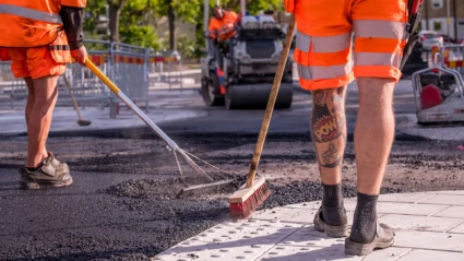 Män i arbetskläder asfalterar väg.