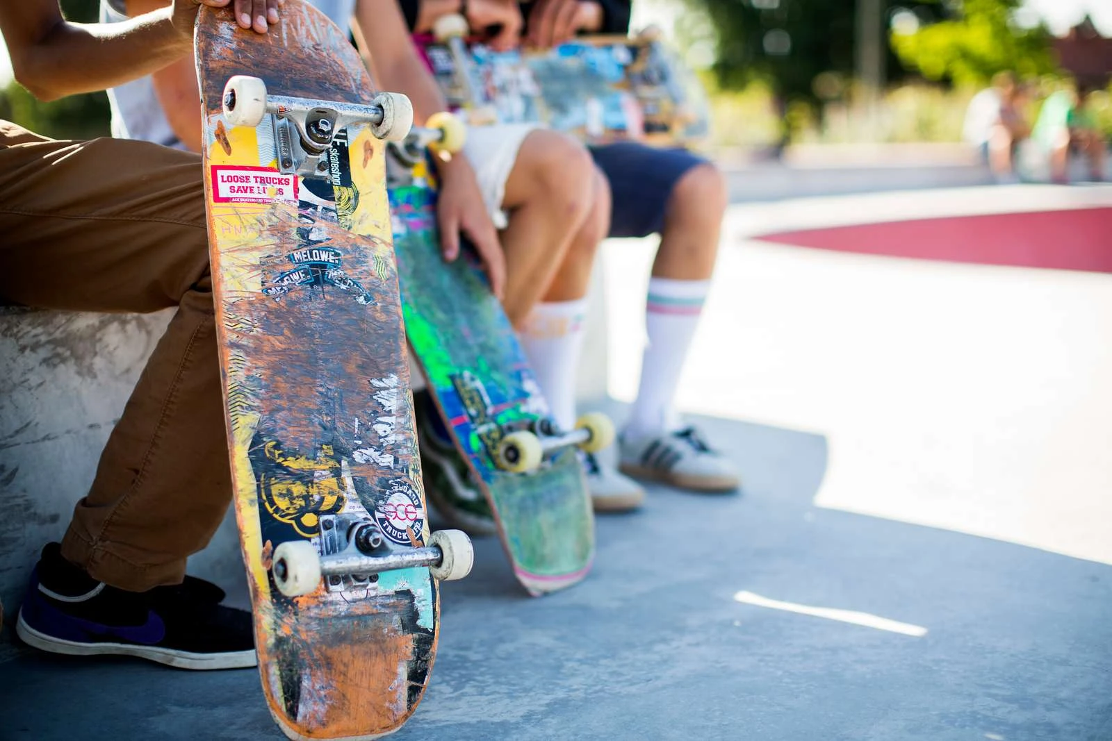 Benen av ungdomar som sitter ner. De håller i skateboards.