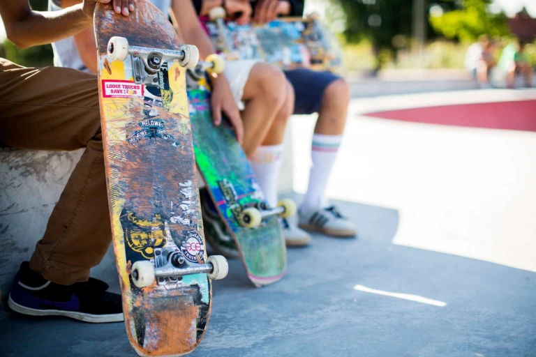 Benen av ungdomar som sitter ner. De håller i skateboards.