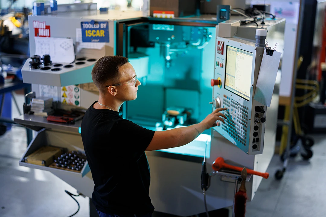 en person står framför en stor instrumentbräda i en fabrik. Personen ser koncentrerad ut.