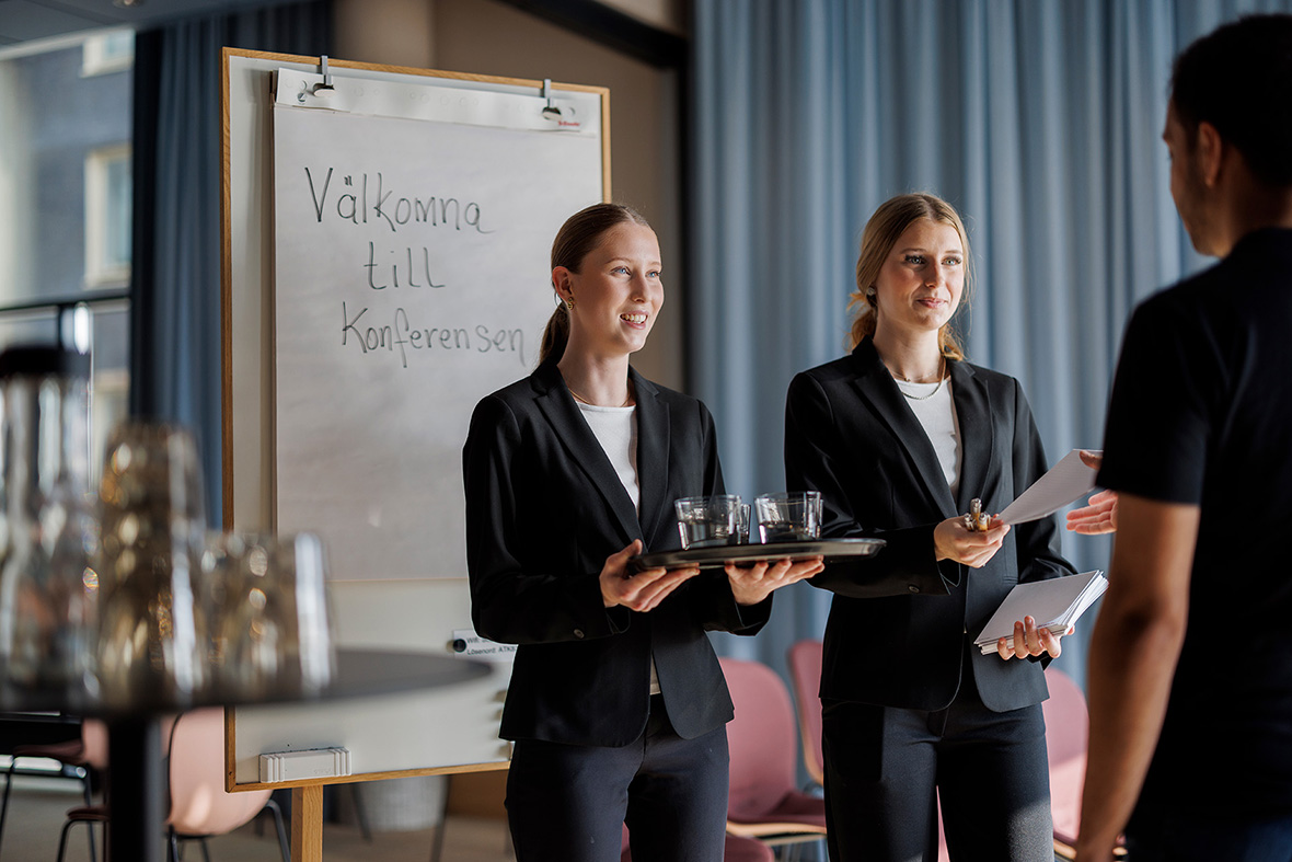 Två unga personer iklädda kostym välkomnar en annan till en konferens