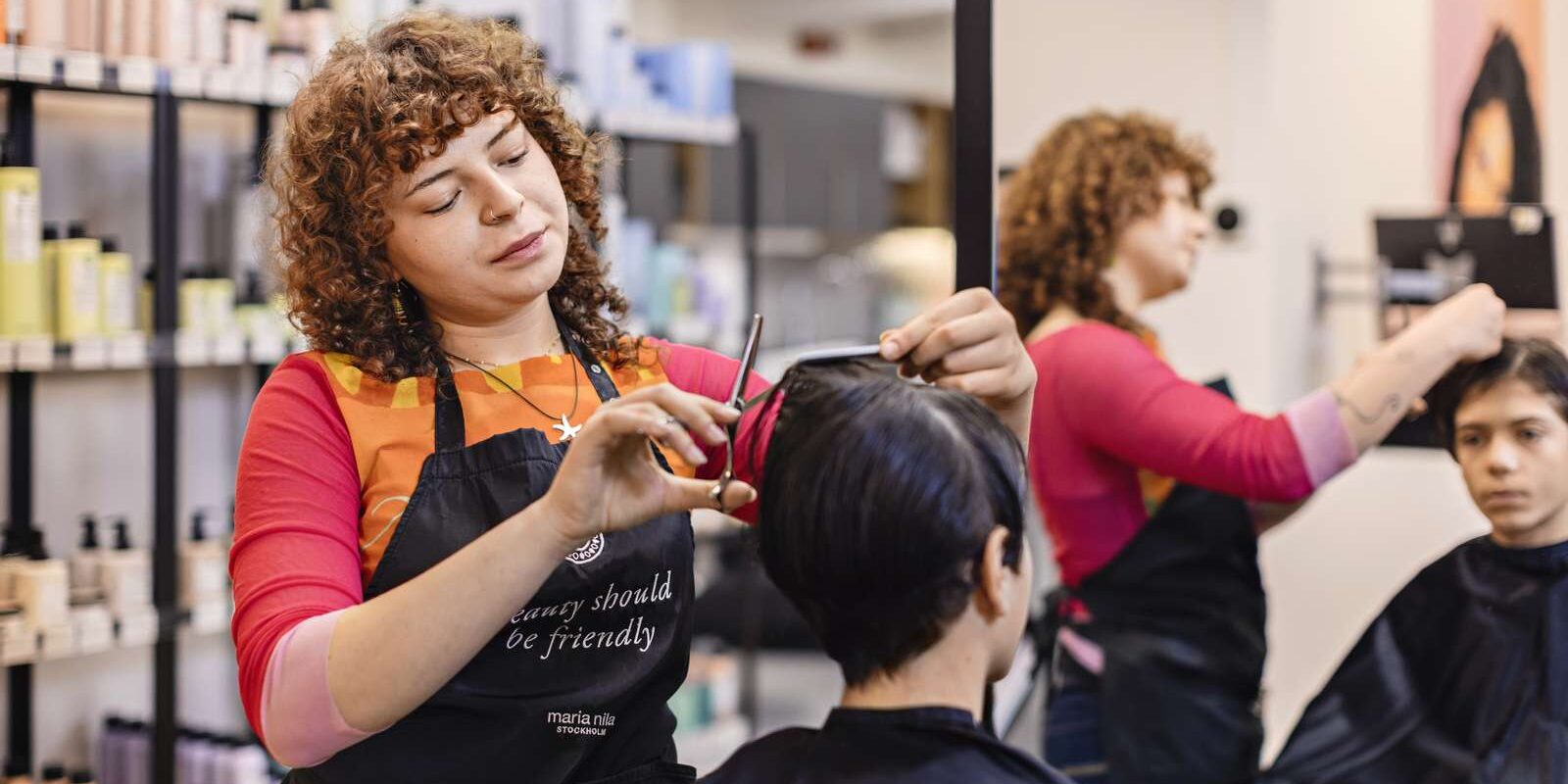 Frisör klipper kund som sitter i en frisörstol i en salong.