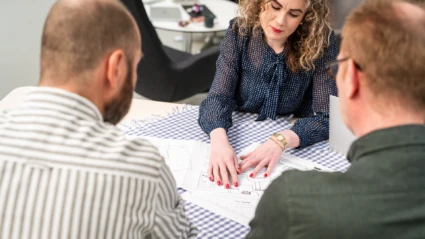 Tre personer runt ett bord med bygglovsritningar