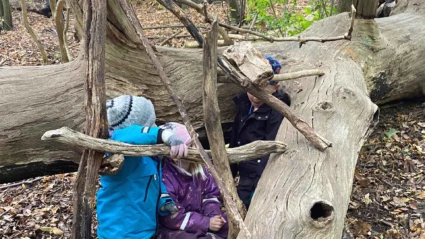 Barn leker i skogen vid en omkullfallen trädstam