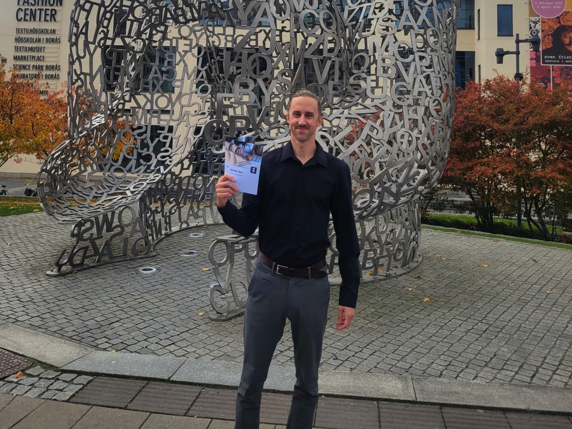 En man står framför ett konstverk och håller en broschyr i handen.