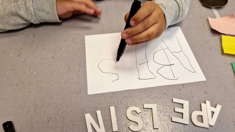 Barn som håller i en penna och skriver ett ord på Äppelgårdens förskola