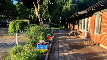 Snöbollsgatans förskola, vy mot fasaden och gården och odlingar i förgrunden. Foto: Förskolan 2024