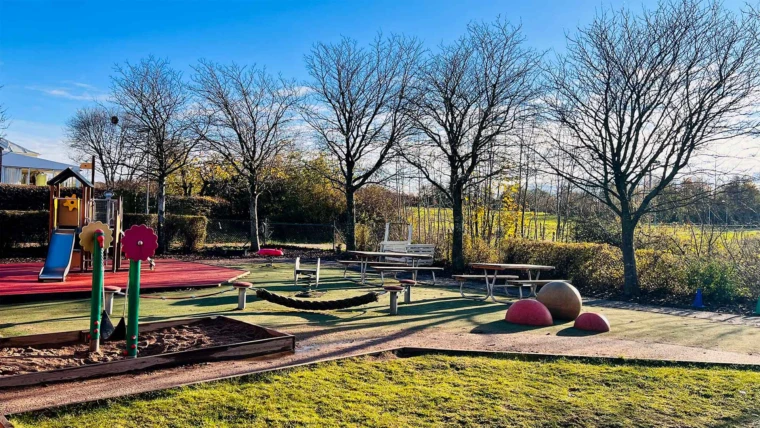 Hästskons förskola. Gården med grönska och lekredskap för olika åldrar. Vy mot hästhagarna bakom förskolan.