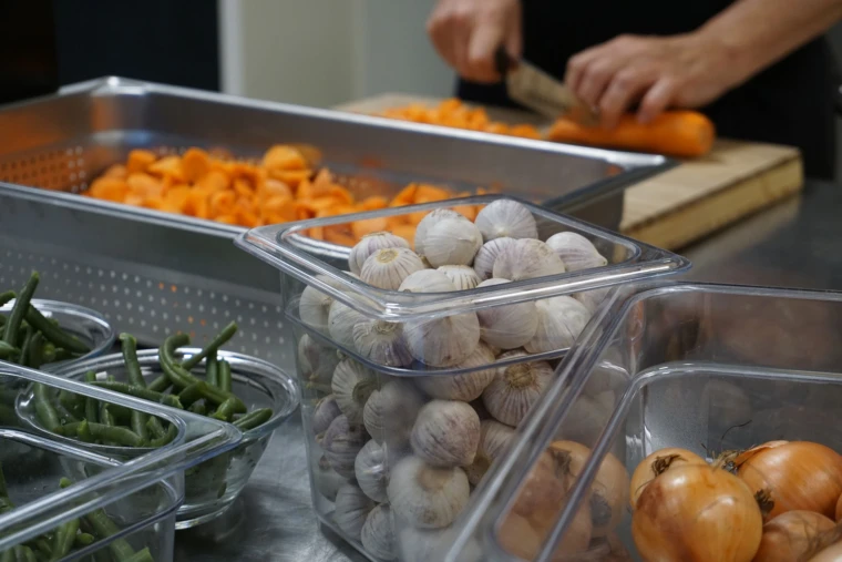 Foto på händer som skär motötter, iförgrunden står skålar och tråg med olika grönsaker och kryddor.