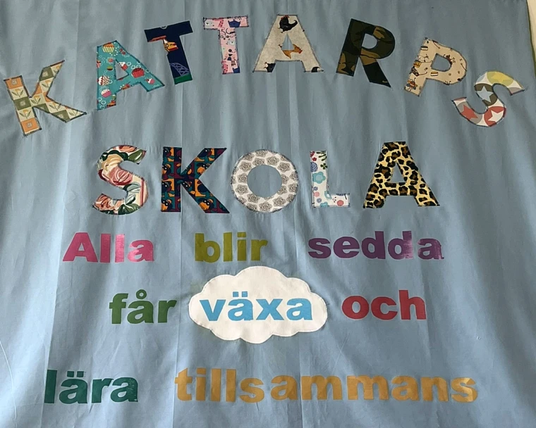Bild med väggbonad och visionstext -Kattarps skola Alla blir sedda får växa och lära tillsammans.
