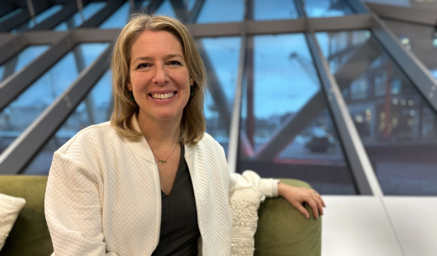 En leende kvinna med vit skjorta sitter i en grön soffa.