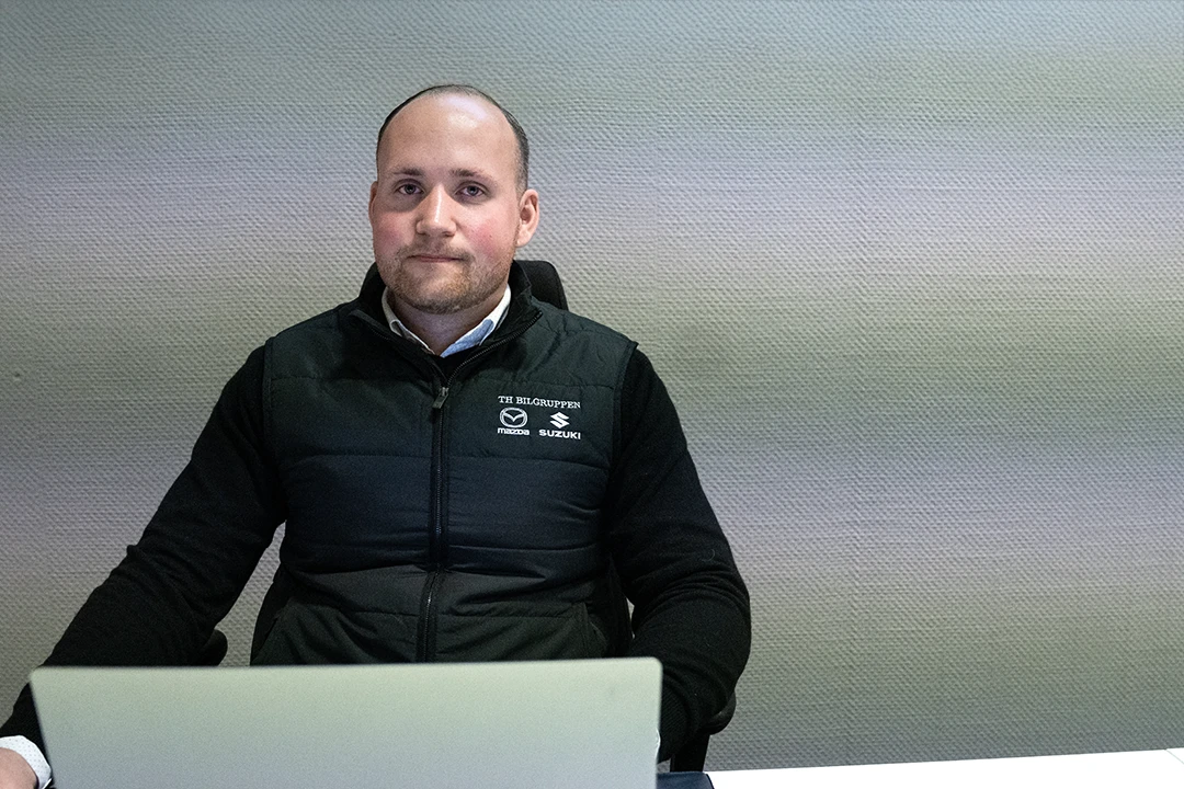 Person sitter bakom dator och ler in i kameran