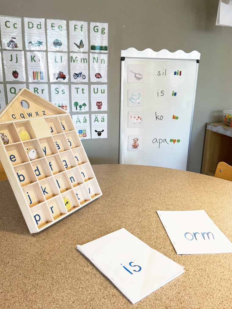 Bild på en tavla med bokstäver. I bakgrunden syns alfabetet och orden sil, is, ko och apa.