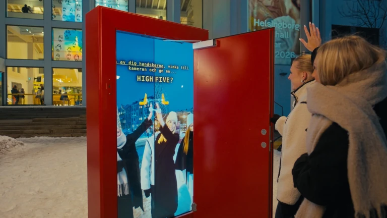 Två personer vid Dunkers kulturhus hälsar på två andra på Gustav Adolfstorg genom Dörren.