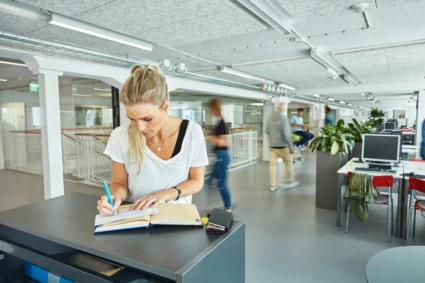 Kvinna som står och skriver vid ett bord på vuxenutbildningens lokaler i Helsingborg.