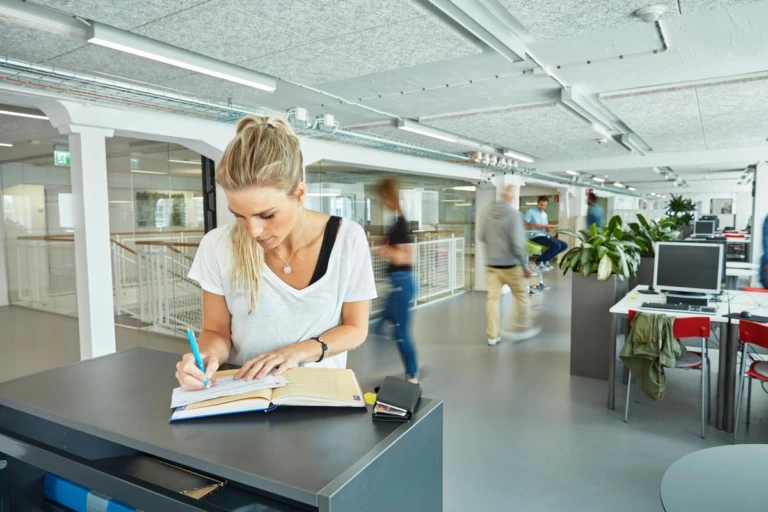 Kvinna som står och skriver vid ett bord på vuxenutbildningens lokaler i Helsingborg.