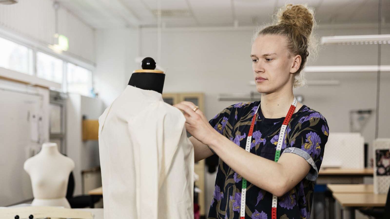 Person nålar ett testplagg på en provdocka. Personen har ett måttband runt halsen