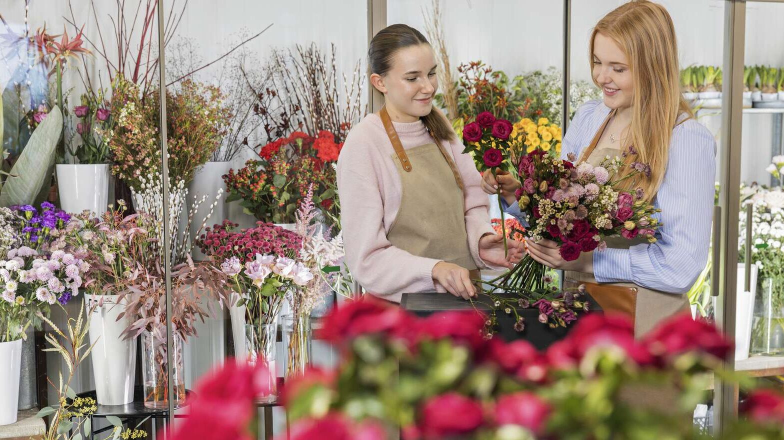 Två personer, iklädda förkläden, gör en bukett tillsammans i en blomsterbutik.