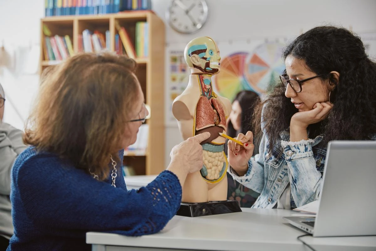 Lärare som berättar om de olika delarna av kroppen för elev i skolsal.