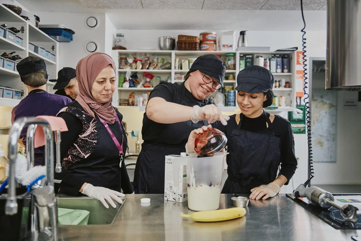 Två elever som förbereder en smoothie med en lärares hjälp i ett kök.
