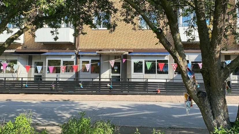Lussebäckens förskolas fasad med färgglada vimplar hängandes i ett träd.