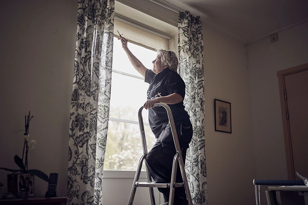 Kvinna står på en stege och fixar en mörkläggningsgardin.