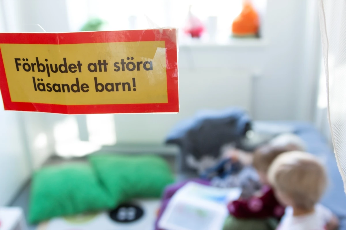 "Förbjudet att störa läsande barn".Barn i bakgrunden av bilden sitter i en soffa och läser bok tillsammans.