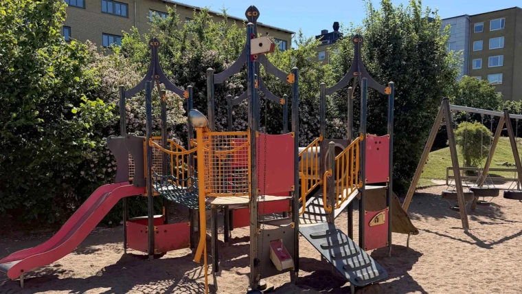 foto på del av gården för de äldre barnen på Ättekulla förskola. En stor röd rutschkana i förgrunden och flera gröna träd och gungor i bakgrunden.