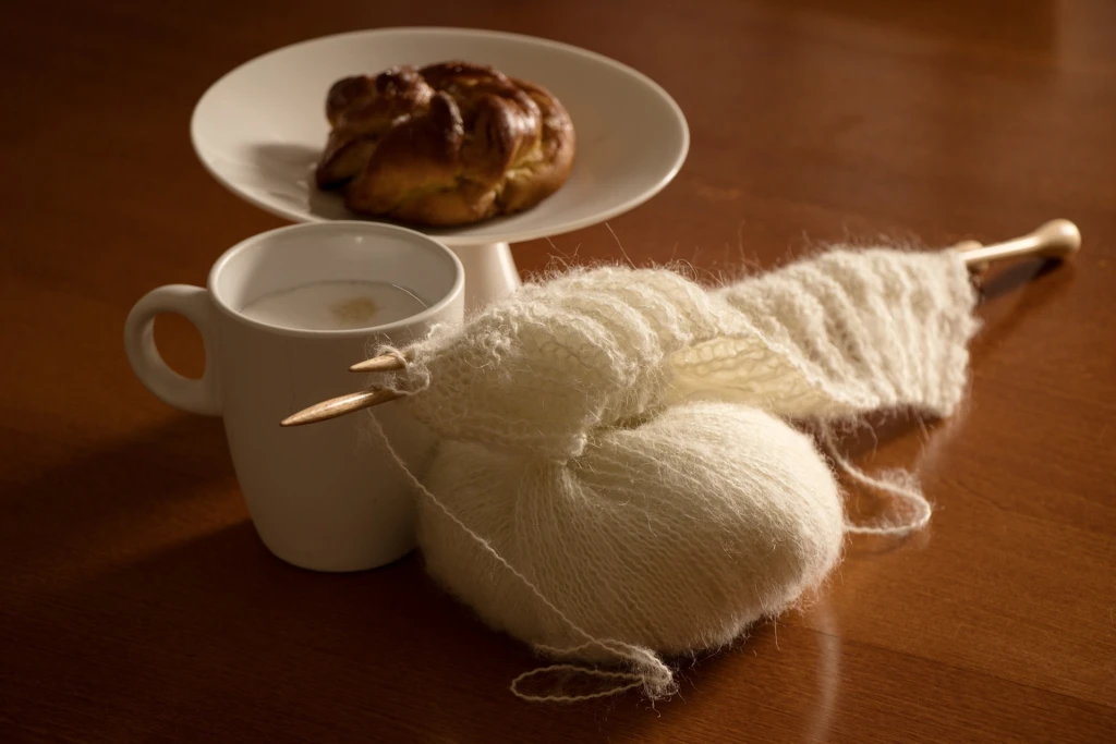 Kaffekopp, kaka på fat och ett garnysta med stickor i.