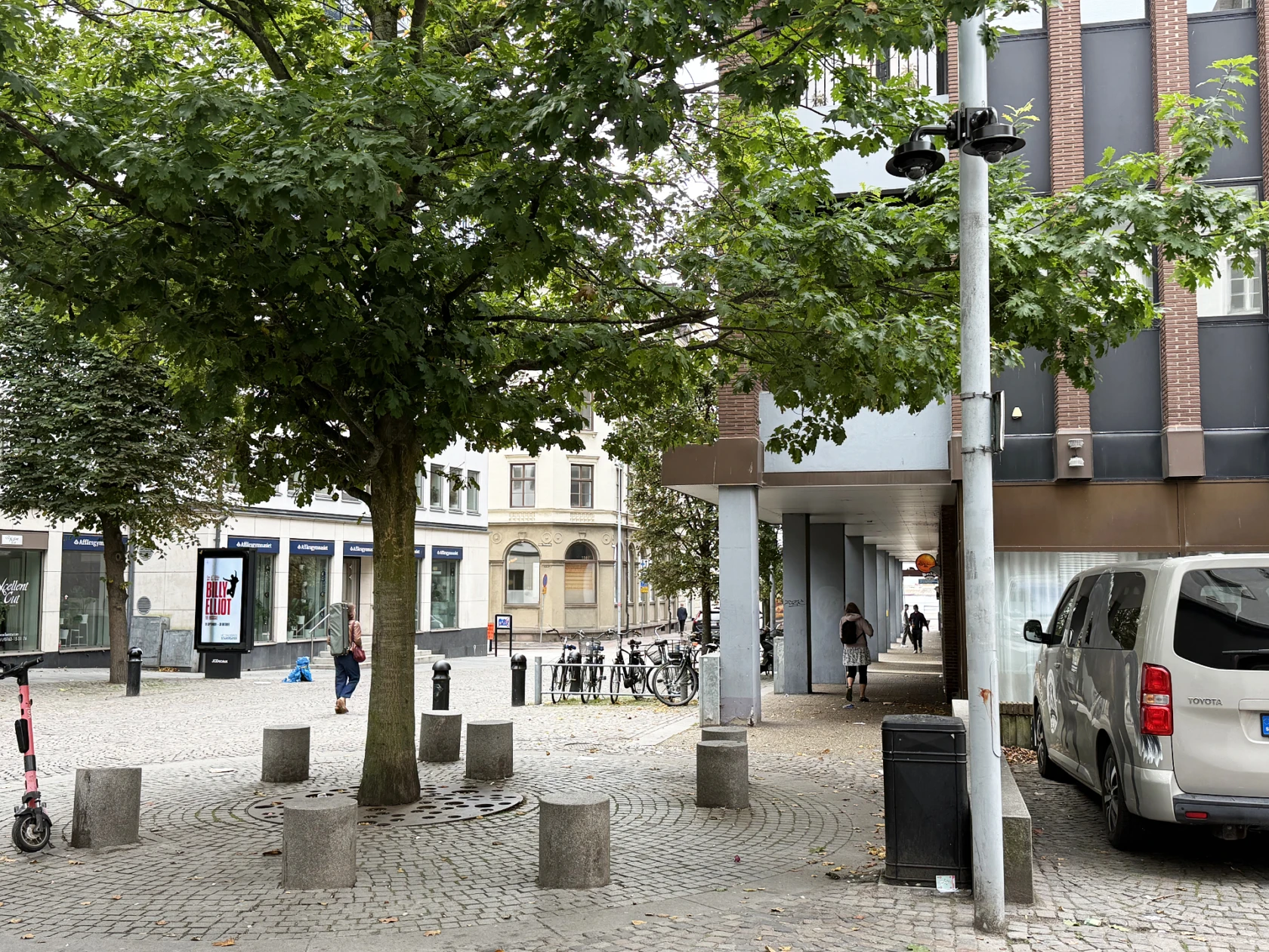 Bevakningskameror på en lyktstolpe intill en plats med träd och sittstenar