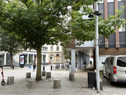 Bevakningskameror på en lyktstolpe intill en plats med träd och sittstenar