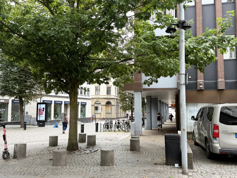 Bevakningskameror på en lyktstolpe intill en plats med träd och sittstenar