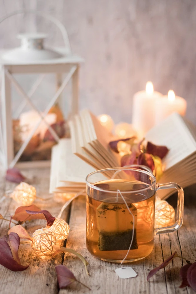 Kopp tea, uppslagen bok, ljuslykta och tända ljus.