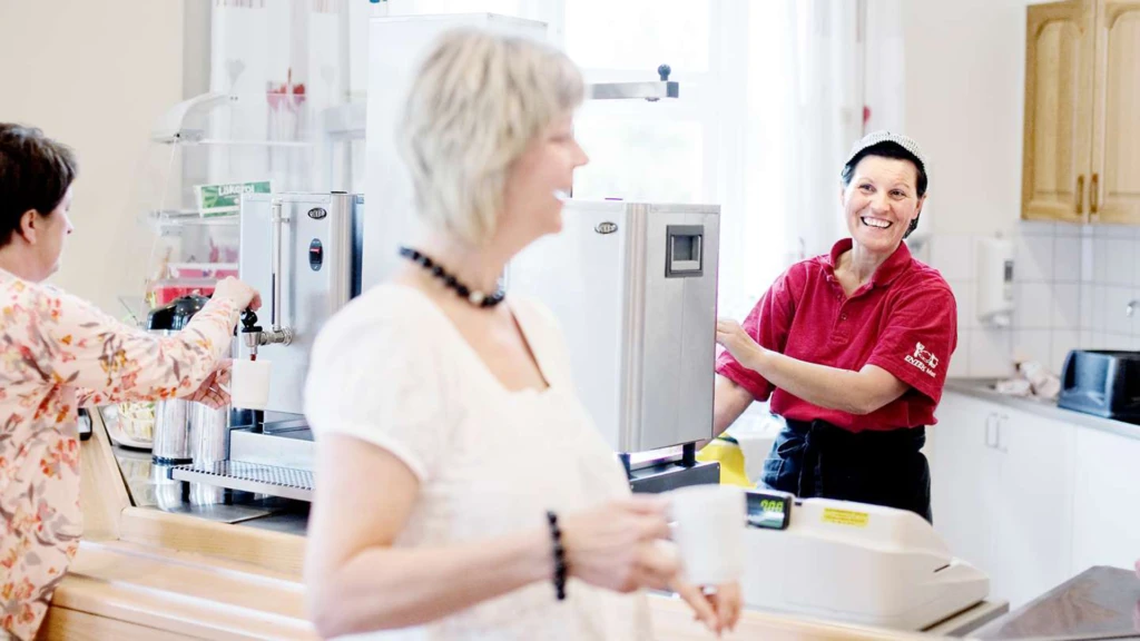 En person som arbetar bakom disken på en matservering ler mot en kund.