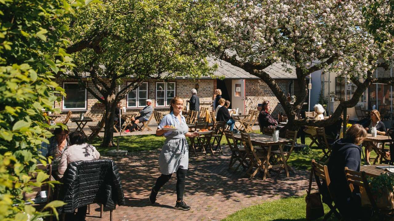 Kvinna går ut med en beställning på ett grönskande trädgårdscafé.