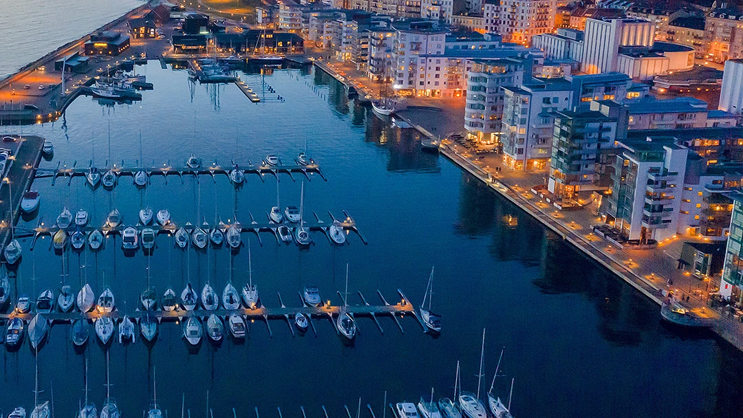 Kvällsbild över norra hamnen. Segelbåtar i hamnen och det lyser fint i fönsterna.