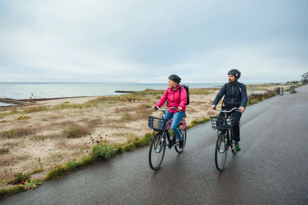 En man och en kvinna cyklar längs strandpromenaden i Helsingborg en höstdag. Båda blickar ut över sundet.