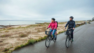 En man och en kvinna cyklar längs strandpromenaden i Helsingborg en höstdag. Båda blickar ut över sundet.
