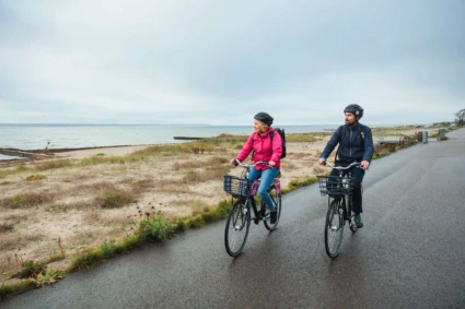 En man och en kvinna cyklar längs strandpromenaden i Helsingborg en höstdag. Båda blickar ut över sundet.