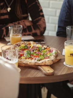Närbild på ett bord där några personer sitter runt. I mitten står en nygräddad pizza och personerna har öl i deras glas.